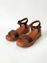 Sandalias de plataforma color chocolate con tira frontal ancha de gamuza y tira al tobillo con hebilla metálica ajustable.