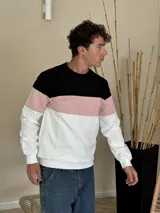 Buzo de cuello redondo con diseño tricolor en bloques horizontales, combinando negro en la parte superior, rosado en el centro y blanco en la parte inferior y mangas.
