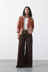 Blazer de gamuza color terracota con bordados decorativos en color crudo en solapas, puños y ruedo. Presenta corte recto, solapas clásicas y cierre frontal con un botón forrado.