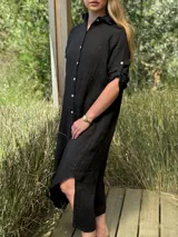 Vestido camisero largo de lino blanco, con cuello camisero, manga corta enrollada y cierre frontal de botones de nácar. Presenta aberturas laterales en el bajo.