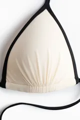Top de bikini de triángulo con copas acolchadas preformadas y diseño fruncido, en color blanco con ribetes negros y tiras ajustables para atar al cuello y la espalda.