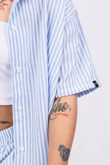 Conjunto de camisa y shorts a rayas verticales celestes y blancas. La camisa es de manga corta y se usa abierta sobre un top blanco.