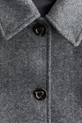 Abrigo de tejido afieltrado color gris oscuro, corte evasé, con cuello solapa y cierre frontal de botones oscuros. Presenta mangas raglán y dos bolsillos delanteros con solapa.