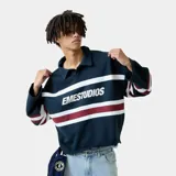 Polo de manga larga color azul marino, con cuello clásico y cierre de botones. Presenta rayas horizontales blancas y bordó en el pecho y las mangas, y el logo "EMESTUDIOS" estampado en blanco en el frente. Tiene un corte holgado.