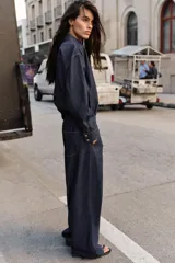 Jeans de tiro alto color azul oscuro, con cintura elástica en la espalda, bolsillos delanteros y bolsillos de plastrón en la espalda. Presenta pernera ancha y cierre frontal con cremallera y botón a presión.