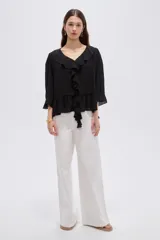 Blusa de poliéster color negro, con diseño holgado, escote en V con solapa y volados que descienden en cascada por el frente. Cuenta con mangas 3/4 con detalles de volados en los puños y en el ruedo.