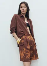 Short de algodón color marrón con estampado de palmeras, diseño recto, pinzas delanteras, bolsillos laterales y cierre con gancho y cremallera.