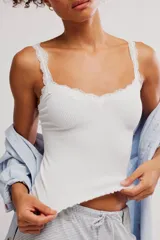 Musculosa blanca de tejido acanalado con detalles de encaje festoneado en el escote y los tirantes, corte ajustado y ruedo con terminación ondulada.