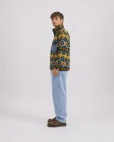 Buzo polar de cuello alto con cierre frontal de botones a presión, confeccionado en fleece sintético. Presenta un estampado geométrico multicolor con predominancia de tonos azules, amarillos y verdes. Incluye un bolsillo frontal tipo cargo con solapa y cierre de botón, además de bolsillos laterales ocultos.