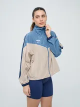 Campera cortaventos Umbro de diseño colorblock en tonos celeste, beige y azul marino, con cuello alto, cierre frontal y bolsillos laterales.