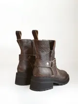 Bota corta de cuero vacuno en color chocolate con efecto desgastado. Presenta una suela track de goma negra, detalle de pulsera desmontable con tachas metálicas y cierre lateral.