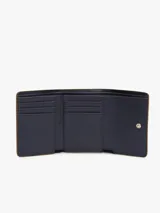 Billetera trifold de Tommy Hilfiger en color marrón, confeccionada en poliuretano con textura granulada. Presenta un diseño plegable con solapa frontal y el logo metálico TH en tono dorado en el centro.