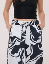 Pantalón ancho negro y blanco con estampado abstracto, cintura elástica con cordón ajustable, bolsillos delanteros con detalles de pompones y corte tobillero.