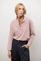 Remera de manga larga en color rosado, con cuello redondo y cierre frontal parcial con botones. Presenta un diseño de corte recto y estilo minimalista.