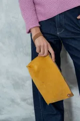 Sobre de cuero agamuzado color mostaza, con cierre de cremallera y logo grabado en el frente.