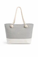 Bolso tipo tote bag con estampado de rayas horizontales grises y blancas, y base lisa color beige. Tiene asas de cuerda color crema anudadas.