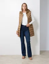 Chaleco largo capitoneado color marrón, con capucha no desmontable y jareta de ajuste. Tiene cierre metálico central, bolsillos inclinados y avíos metálicos con logo. Incluye bolsa autoportante.