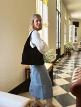 Bolso tipo tote bag negro de cuero, con costuras a la vista y manijas cortas.