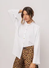 Camisa blanca de cuello redondo con frunces, abotonada y de manga larga con puño abierto.