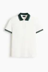 Polo de manga corta en piqué de algodón, color blanco con cuello y bordes de mangas en color verde oscuro con detalles de líneas blancas. Presenta tapeta con botones.