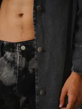 Trench largo de denim gris lavado, de silueta recta y amplia, con solapas amplias, mangas largas y botonadura frontal.