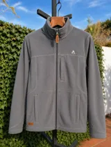 Campera de polar azul marino con cierre frontal completo, cuello alto, bolsillos laterales y un bolsillo vertical en el pecho. Presenta detalles en cuero sintético en el tirador del cierre y una etiqueta de marca en el ruedo.