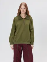 Buzo verde militar de algodón suave, de calce oversize, con cuello alto y cierre frontal parcial metalizado. Cuenta con bolsillos laterales con cierre y puños y ruedo elastizados.