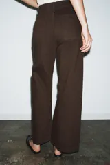 Jeans de tiro alto confeccionados en mezcla de algodón, con diseño de pierna ancha y costura marcada en el delantero. Presenta cintura con trabillas, cierre frontal con cremallera, botón y gancho metálico, y bolsillos de plastrón en la espalda.