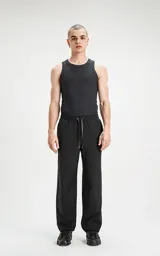 Pantalón negro de tejido técnico impermeable, corte recto y holgado, con elástico en cintura y puños. Presenta cordones ajustables con estampado repetitivo en la bragueta y un pequeño parche cuadrado con un logo de tijeras en el muslo derecho.