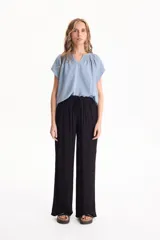 Blusa negra de manga corta, confeccionada en tela crepé, con detalle de fruncido en el escote redondo y pequeña abertura frontal en V.