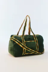 Bolso de viaje grande color verde oscuro con acolchado de pespuntes verticales. Cuenta con cierre superior con tirador de borla, doble asa de hombro y correa regulable con detalles a cuadros en tonos amarillos y blancos.