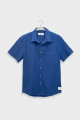 Camisa azul de manga corta confeccionada en algodón ligero con textura waffle. Presenta un corte cuadrado, bolsillo en el pecho y botones de coco con el logo de Polonio.