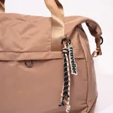 Bolso tipo tote color marrón claro, con doble asa corta color dorado y correa larga ajustable. Incluye un bolsillo externo con cierre y un dije con la palabra 'traveller'.