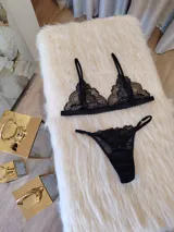 Conjunto de lencería compuesto por un bralette de encaje con breteles regulables y una tanga regulable con corte cola less. Ambas piezas presentan un diseño de encaje floral negro.