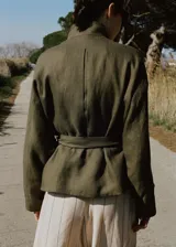 Chaqueta de lino color verde militar, diseño oversize con cuello alto, cierre oculto, manga larga con puño abotonado y cinturón ajustable en la cintura.