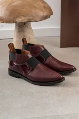 Zapato tipo botineta de cuero color bordó con textura grabada, diseño de punta fina y detalles de elásticos laterales en color negro.