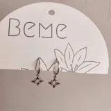 Aros plateados tipo argolla con dije colgante en forma de estrella de ocho puntas con incrustaciones de strass.