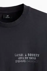 Remera de algodón color gris oscuro con cuello redondo y estampado pequeño en el pecho con texto en color blanco.
