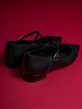 Chatitas negras de cuero sintético con punta charol y tira con hebilla.