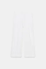 Pantalón fluido de tiro alto en color blanco, con cintura elástica y bolsillos delanteros. Presenta un diseño de pierna ancha y bajo acabado con detalle de lazada.