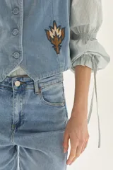 Camisa a rayas verticales de calce recto, con cuello clásico y mangas abullonadas con detalles de frunces y lazos en los puños. Presenta un pequeño bordado en el pecho.