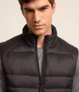 Chaleco masculino deportivo tipo puffer, color negro, con cuello alto, gajos acolchados y cierre delantero con cremallera.