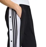 Pantalon deportivo Adidas modelo Adibreak, color negro con franjas laterales blancas y botones a presión. Presenta el logo de la marca y diseño de tres tiras icónico en los costados.