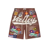 Short baggy de jean marrón con parches bordados coloridos, cordones colgantes en la cintura y aplicación de texto en chenille con tachas y brillos.