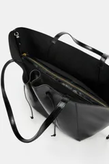 Bolso tipo shopper de efecto arrugado y acabado brillante en color negro, con detalles fruncidos en el centro, cordones colgantes en los laterales y doble asa para el hombro.