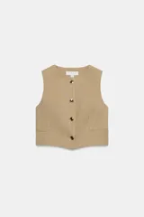 Chaleco corto de color beige con diseño de rayas sutiles, cuello redondo, sin mangas y cierre frontal con botones metálicos dorados. Presenta falsos bolsillos ribeteados en el delantero.