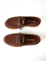 Sandalias de cuero gamuzado color marrón chocolate, diseño tipo huarache con tiras entrelazadas, tira en el empeine, talón cerrado y hebilla metálica de ajuste lateral.