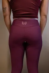 Calza deportiva larga color morado oscuro, tiro alto, con pretina blanca y logo de alas bordado en blanco en la parte trasera de la cintura.