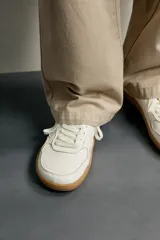Zapatillas deportivas barefoot de hombre elaboradas en piel. Diseño en color blanco con detalles en negro y beige en el talón, y suela plana de goma marrón.