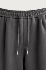 Pantalón jogger de corte relajado confeccionado en tejido de algodón compacto con elasticidad. Presenta cintura elástica ajustable con cordón, bolsillos laterales, bolsillos cargo con solapa en las piernas y detalle de pliegues en las rodillas.